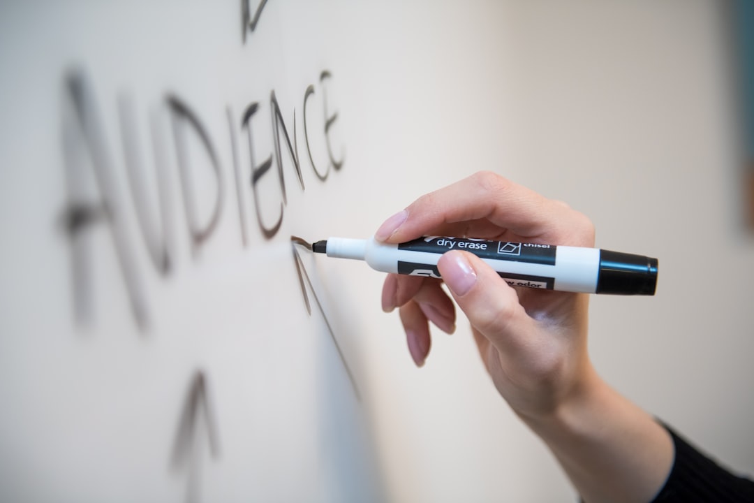 A woman's hand writing the word audience on a whiteboard, with arrows.