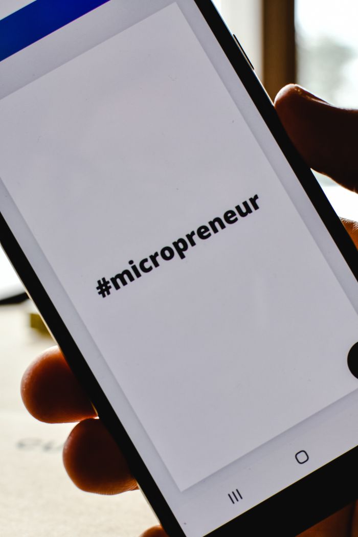 Gros plan sur une main tenant un smartphone dont l’écran affiche le hashtag #micropreneur, illustrant l’esprit d’entrepreneuriat.